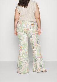 Los pantalones con estampado floral presentan diseños botánicos coloridos sobre un fondo claro, piernas acampanadas y una etiqueta de cuero marrón en la parte trasera de la cintura.