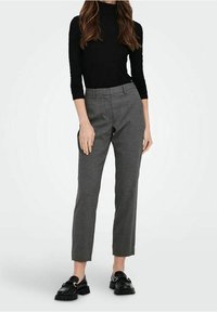 Pantaloni grigi su misura con vestibilità slim e dettagli di piega, abbinati a un dolcevita nero e mocassini neri con un accento dorato.