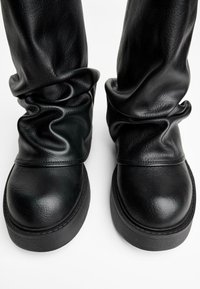 Zwarte leren laarzen met een slouchy ontwerp, voorzien van een gladde textuur, ronde neuzen en een dikke zool voor stabiliteit.