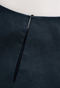 Dark blue linen garment featuring a button at the neckline and a vertical slit detail. The texture is smooth with a slight sheen.