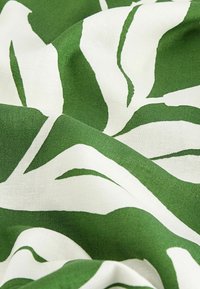 Gros plan sur un tissu vert et blanc avec un grand motif de feuille abstrait, présentant une texture visible et des plis.