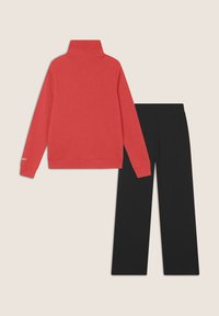 Maglione a collo alto in cotone rosso abbinato a pantaloni neri a gamba dritta. Il top presenta un collo alto e maniche lunghe.