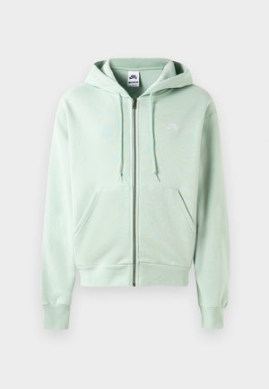 Sweat à capuche zippé vert clair en tissu doux, avec une poche avant, un capuchon à cordon de serrage et un petit logo blanc sur la poitrine gauche.