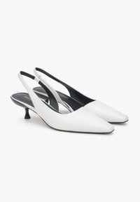 Białe skórzane szpilki typu slingback z wydłużonym noskiem, niskim czarnym koturnem i regulowanym paskiem z tyłu. Gładka tekstura i minimalistyczny design.