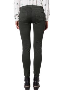 Vaqueros skinny verde oscuro hechos de tejido elástico, con dos bolsillos traseros y una cintura de altura media. Llevados con botas negras hasta el tobillo.