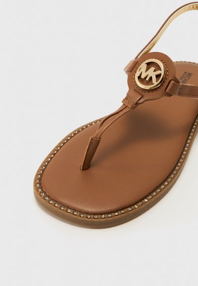 Brun läderflip-flopsandaler med en cirkulär guldsymbol, en pärlbesättning och en slät yta på fotbädden.