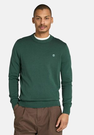 Donkergroen gebreid vest met een ronde hals, geribbelde mouwen en onderrand, en een klein logo op de borst, gecombineerd met een paarse broek.
