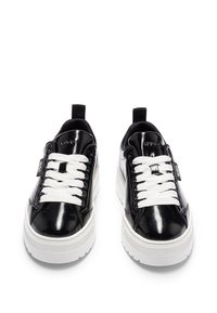 Schwarze Lackledersneaker mit weißen Schnürsenkeln und einer Plateausohle. Mit einem Logo auf der Zunge und einer strukturierten weißen Gummi-Außensohle.