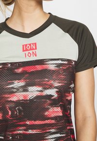 Sportovní dres s krátkým rukávem vyrobený z prodyšného materiálu, s přechodovým designem v červené a černé barvě a šedým panelem na límci.