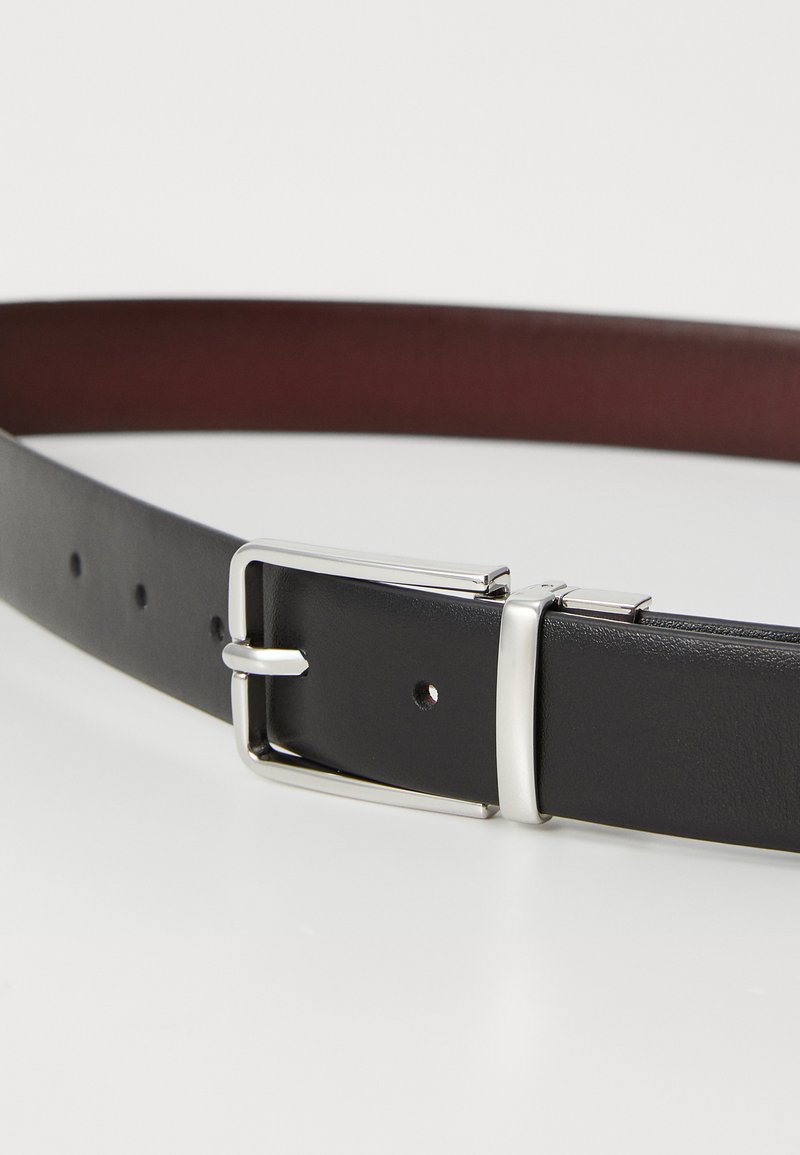 Cintura in pelle nera con finitura liscia, fibbia rettangolare argentata e multiple fori per la regolazione. L'interno mostra un colore bordeaux.