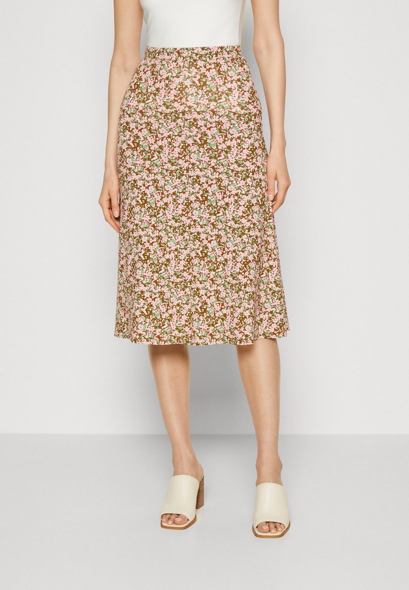 Jupe midi florale brune avec des motifs roses et verts. Tissu doux et léger avec une taille cintrée et une coupe évasée. Associée à des mules à talons beiges.