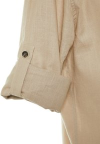 Manche de chemise en lin beige avec un poignet roulé maintenu par une patte boutonnée, montrant la texture du tissu et les détails des coutures.