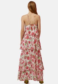 Maxikleid mit floralen Schichten und Rüschen. Weißer Stoff mit rosa und grünen Rosen verziert. Offener Rücken mit dünnen Trägern und einer Bindeschließung.