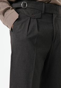 Zwarte broek met visgraatmotief met plooien, een knoopsluiting en een grijze riem met zilverkleurige gespen en contrasterende stiksels.