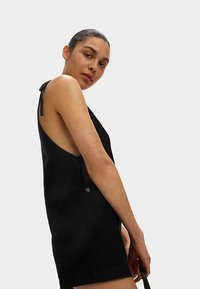 Schwarzes ärmelloses Kleid mit offenem Rückendesign, dünnen Trägern, einem Knopfdetail an der Seite und glatter Textur.