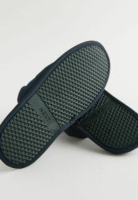 Chaussons bleu marine avec une semelle en caoutchouc texturée. Présentent un dessus lisse et une marque en relief. La semelle a un motif en diamant pour une meilleure adhérence.