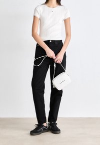 Biała, prążkowana koszulka, czarne spodnie z wysokim stanem, czarne trampki. Mała biała torba na ramię z zamkiem błyskawicznym, z logo "Tommy Hilfiger".