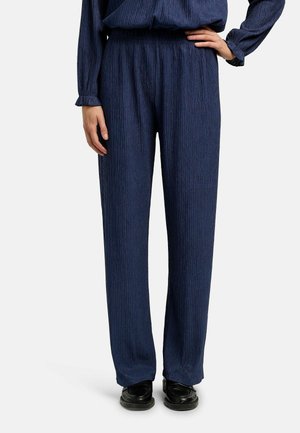 Granatowe plisowane spodnie zestawione z dopasowanym długim rękawem i czarnymi skórzanymi butami na osobie stojącej prosto.