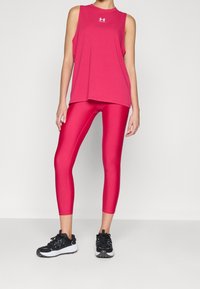 Mujer con una blusa sin mangas de color rosa brillante y leggings rosas a juego, con zapatillas deportivas negras y blancas, de pie contra un fondo liso.