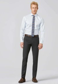 Chemise bleu clair à manches longues, associée à un pantalon noir ajusté et une cravate à motifs dans des teintes de bleu et de marron. Ceinture et chaussures marron.