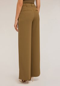 Brede broekspijpen in kaki met een gladde textuur, voorzien van achterzakken en een hoge taille, gecombineerd met naakte hoge hakken.