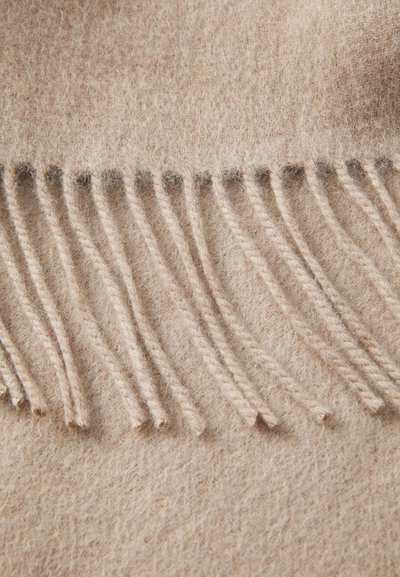 Couverture en laine beige avec bord frangé, présentant une texture douce et une apparence uniforme et duveteuse. Les franges sont soigneusement tissées et régulières.