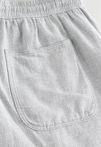 Tissu gris clair avec ceinture élastique et une poche carrée cousue avec un patch, sur un pantalon ou un short à texture douce.