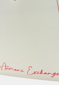 Borsa bianca texturizzata con logo rosso "Armani Exchange", caratterizzata da linee morbide e un design minimalista. Nessun hardware o accento visibile.
