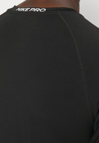 Czarna koszulka sportowa Nike Pro z okrągłym dekoltem, krótkimi rękawami i płaskimi szwami, które redukują otarcia. Logo umieszczone z tyłu.