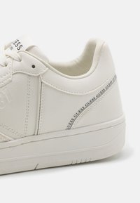 Sneaker bianca in pelle con una superficie liscia, caratterizzata da una forma arrotondata, lacci piatti bianchi e un accento del logo sul lato.