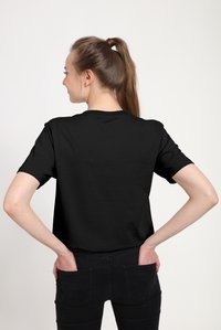 Sort kortærmet T-shirt med rund halsudskæring, lavet af bomuld. Bagsiden er ensfarvet og T-shirten har en afslappet pasform. Kombineret med sorte bukser.