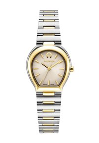 Zelta un sudraba nerūsējošā tērauda pulkstenis ar unikālu asaru formas korpusu, teksturētu šampanieša krāsas ciparnīcu, zelta stundu rādītājiem un Šveices ražojuma marķējumu.