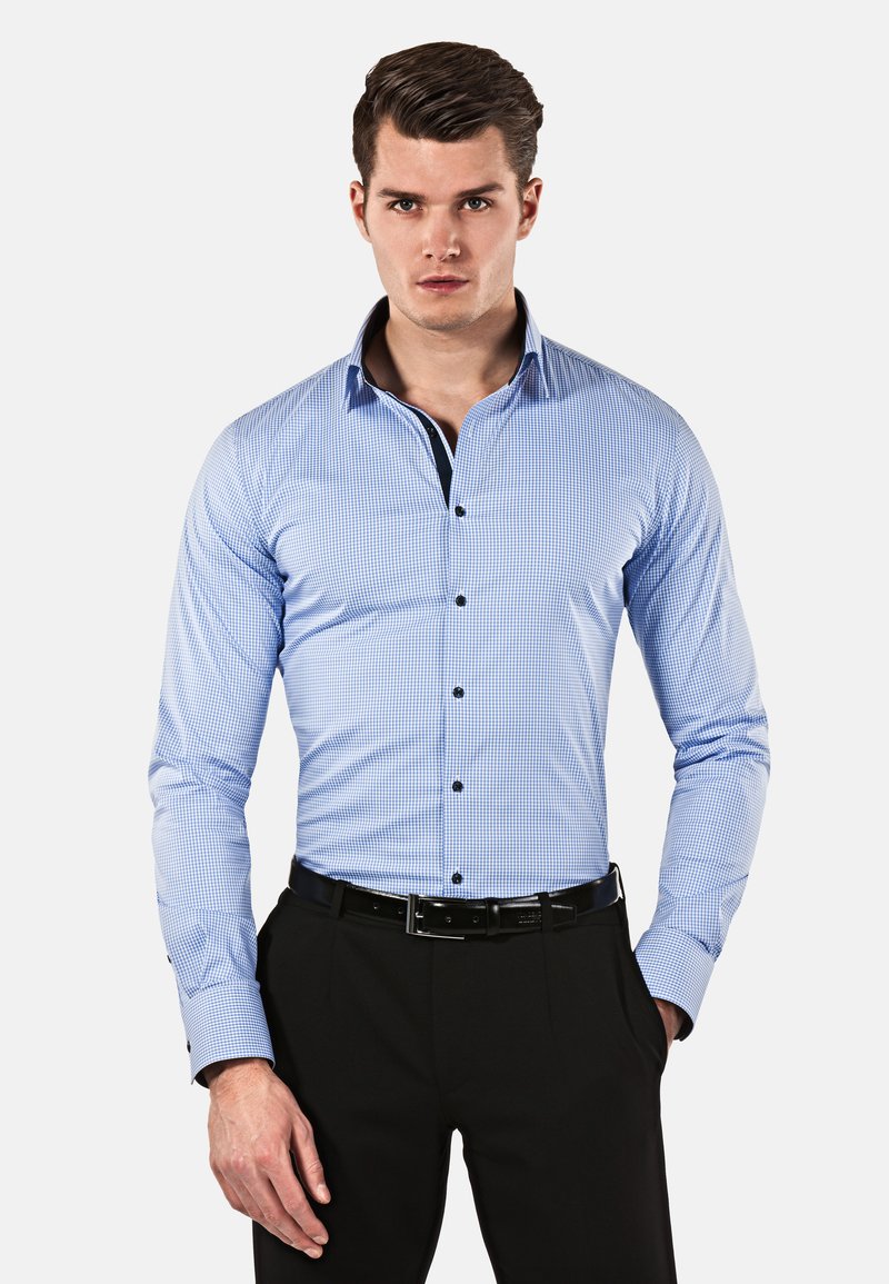 Camicia a quadretti blu e bianchi con colletto alla francese, bottoni neri e maniche lunghe, abbinata a pantaloni eleganti neri e a una cintura.