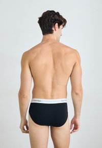 Chiloți negri din bumbac cu un tiv elastic alb pe care este inscripționat logo-ul "Calvin Klein", văzuți din spate pe un fundal neutru.