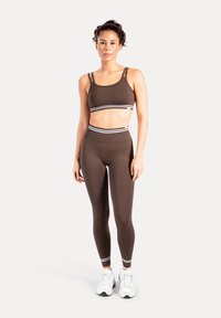 Ensemble sportif marron composé d'un crop top à fines bretelles et d'un legging taille haute assorti. Les deux pièces sont décorées de bandes accentuées blanches.