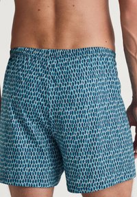 Heren zwemshorts met een blauw en teal geometrisch patroon. Elastische tailleband, lengte tot halverwege de dij en lichtgewicht stof met een gladde textuur.