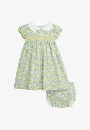 Ziedu kleita ar dzeltenu fonu un rozā un zilām ziedēm, īsām piedurknēm un balto viļņoto apkakli, iekļaujot atbilstošas biksītes.