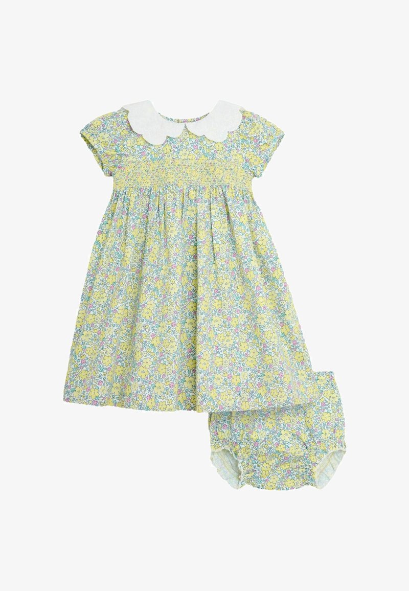 Blommig klädset med en gul bakgrund och rosa och blå blommor, korta ärmar och en vit vågig krage, inkluderar matchande byxor.