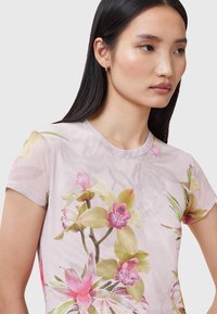 Blomster top med korte ærmer i transparent lys pink stof, med store orkidé tryk i nuancer af pink og grøn, samt en rund halsudskæring.