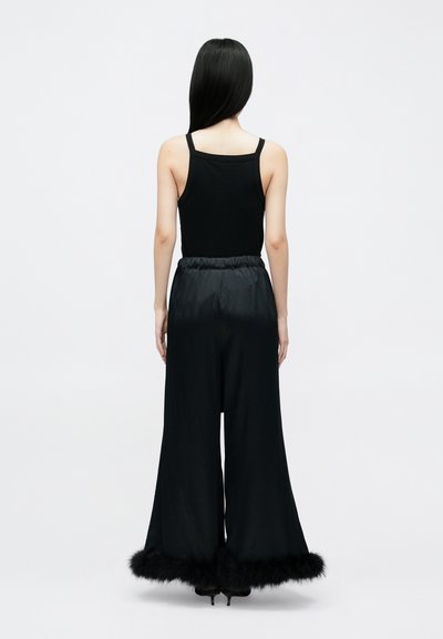 Crna majica bez rukava i široke hlače s mekanim crnim krznom umjetnog krzna na rubovima. Glatka, satenska tkanina s elastičnim pojasom.