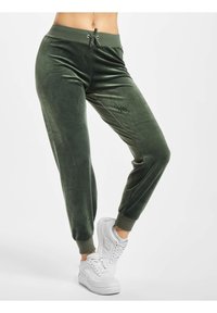 Gröna velourbyxor med elastisk midja, dragsko och åtsittande mudd, kombinerat med vita sneakers. Slät yta, slim fit.