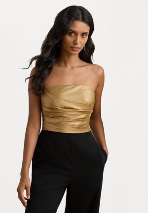 Top dorato senza spalline con design in tessuto arricciato, abbinato a pantaloni neri a vita alta con tasche laterali e texture morbida.