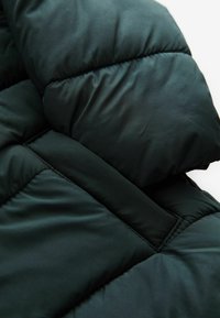 Mørkegrøn pufferjakke stof med quiltet design, glat tekstur og tyk polstring med en fremtrædende sømdetalje.
