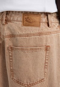 Τζιν μπεζ ντένιμ με δερμάτινο έμπλαστρο με λογότυπο στο πίσω μέρος, που διαθέτει στάνταρ τσέπη και διακριτική διαγώνια υφή.