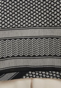 Tessuto in bianco e nero con motivi geometrici, tra cui il motivo scozzese e zigzag, con una texture liscia e tessuta.