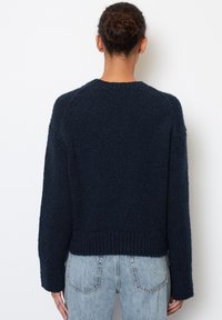 dunkelblauer Strickpullover mit strukturiertem Finish, verkürztem Design und geripptem Saum. Lange Ärmel mit leicht fallenden Schultern.