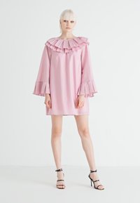 Ροζ, κοντομάνικο φόρεμα με γαζί στο λαιμό και πλισέ μανίκια καμπάνα. Λιώμα ύφασμα, χαλαρή εφαρμογή, μήκους μέχρι το γόνατο. Μάυρα πέδιλα με τακούνι.