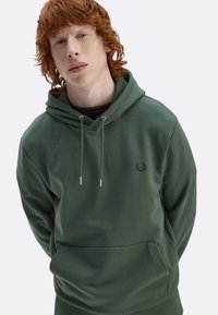 Felpa con cappuccio verde in tessuto morbido, con tasca frontale, coulisse e logo scuro sul petto; texture liscia e vestibilità comoda.