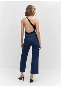 Bodysuit negro de un solo hombro y jeans de cintura alta de pierna ancha en azul oscuro. La tela parece suave con un sutil brillo, combinada con tacones de aguja.
