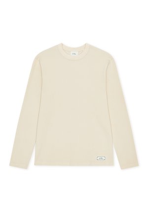 T-shirt beige à manches longues avec col rond et une petite étiquette rectangulaire près de l'ourlet inférieur sur fond blanc.